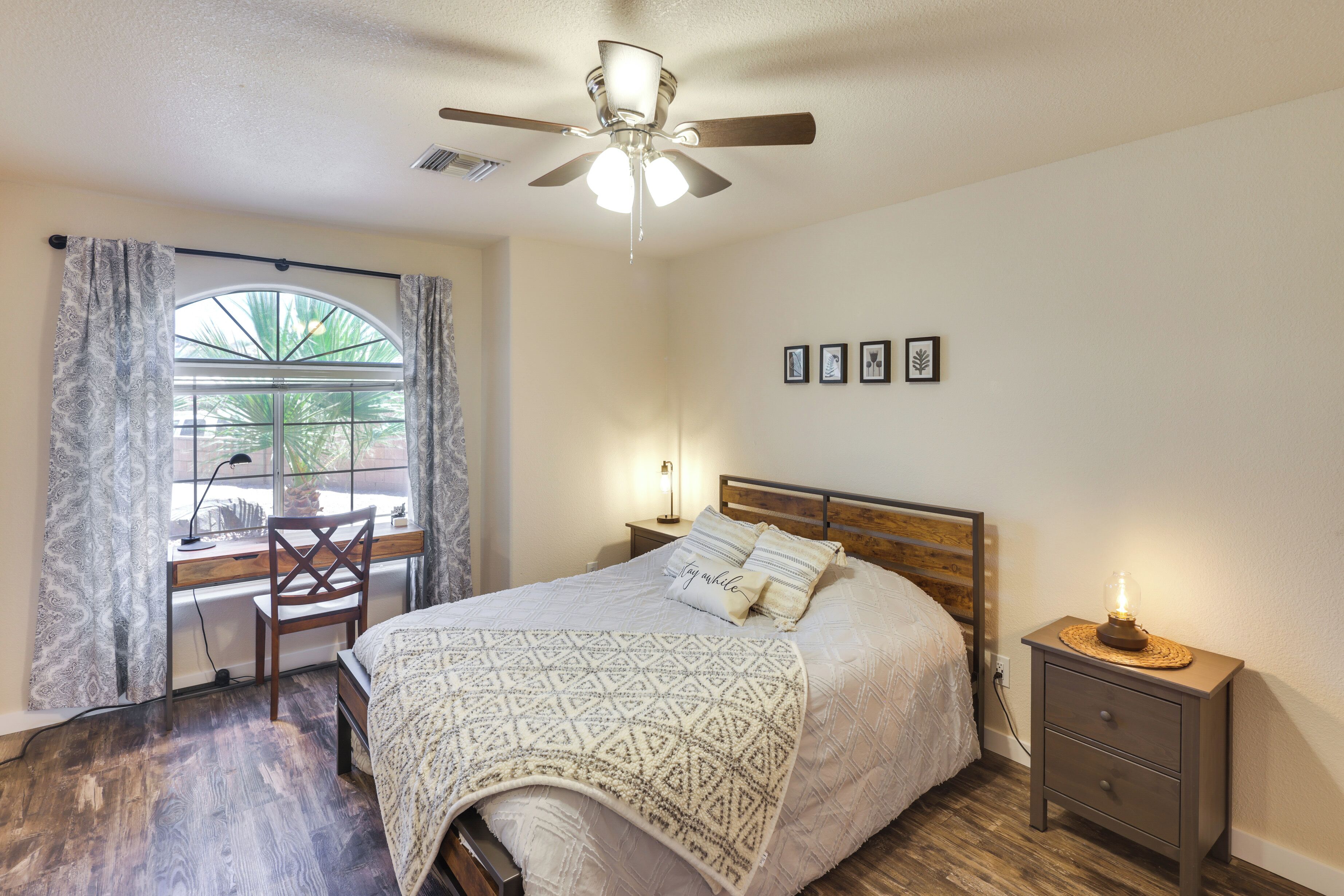A bedroom with a bed, a desk, a chair, a nightstand, and a ceiling fan.