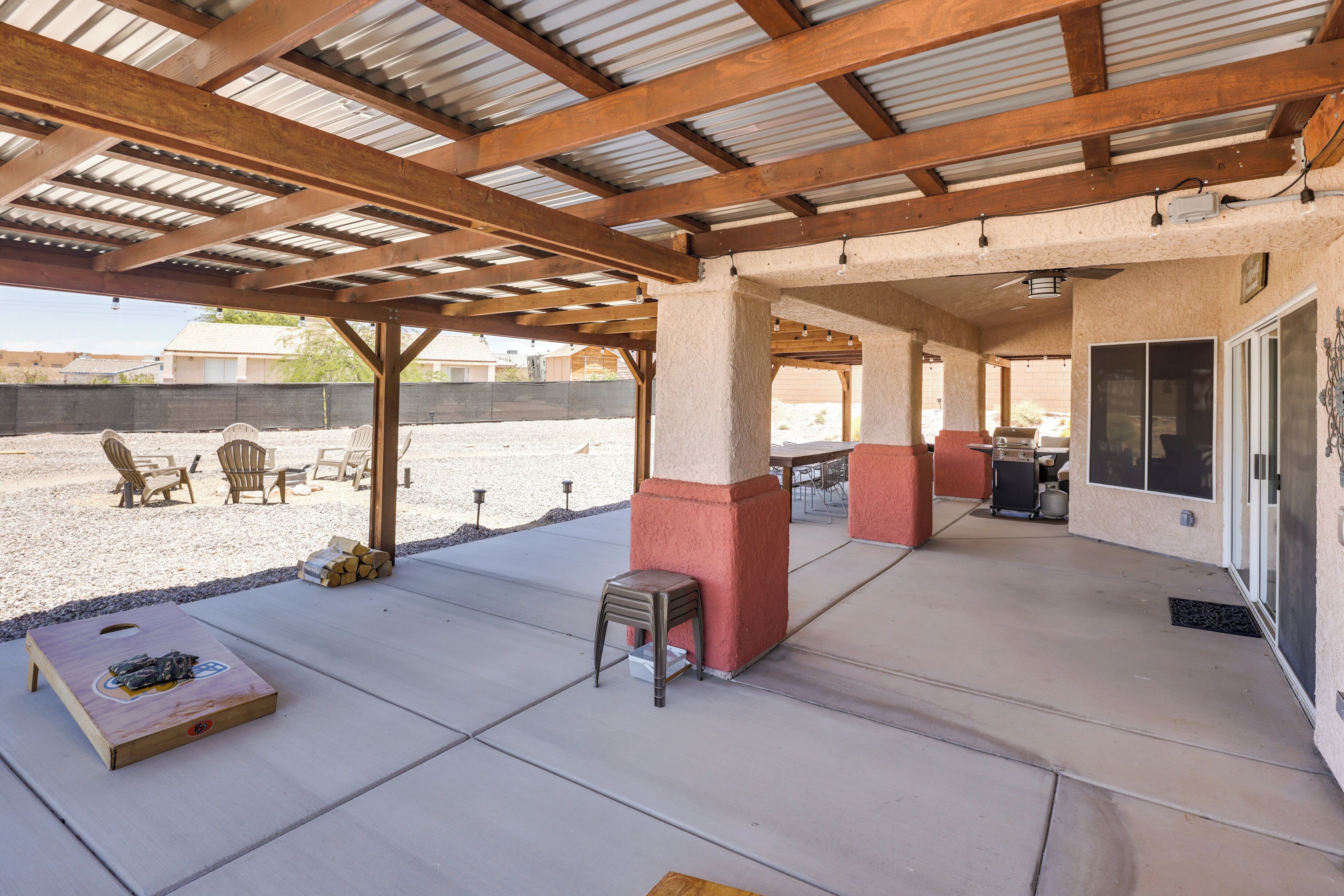 Un patio al aire libre con zona de estar cubierta, una mesa de madera y una parrilla.