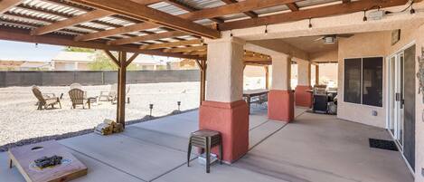 Un patio al aire libre con zona de estar cubierta, una mesa de madera y una parrilla.