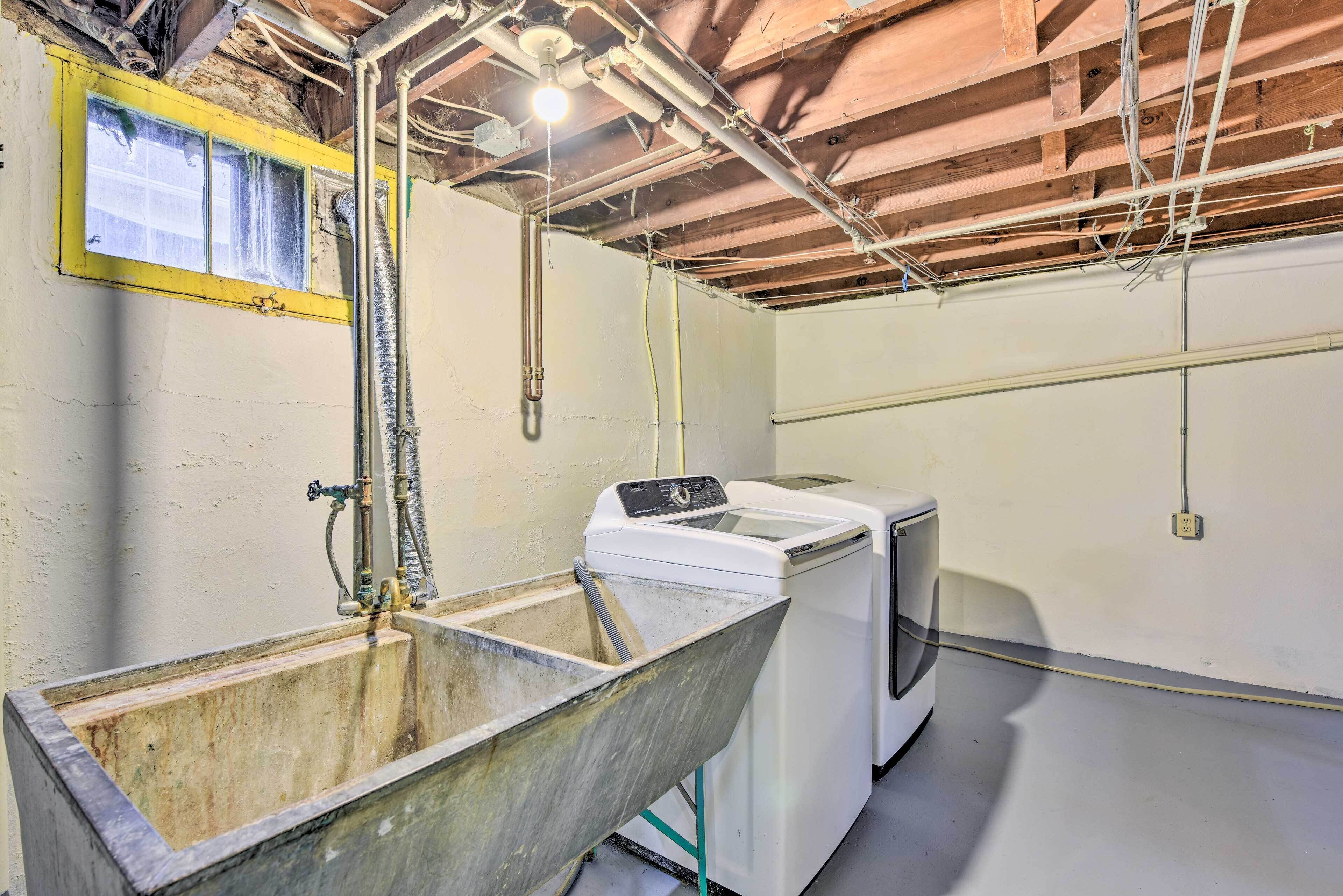 A laundry room with a large metal sink, a washing machine, and exposed ceiling pipes.