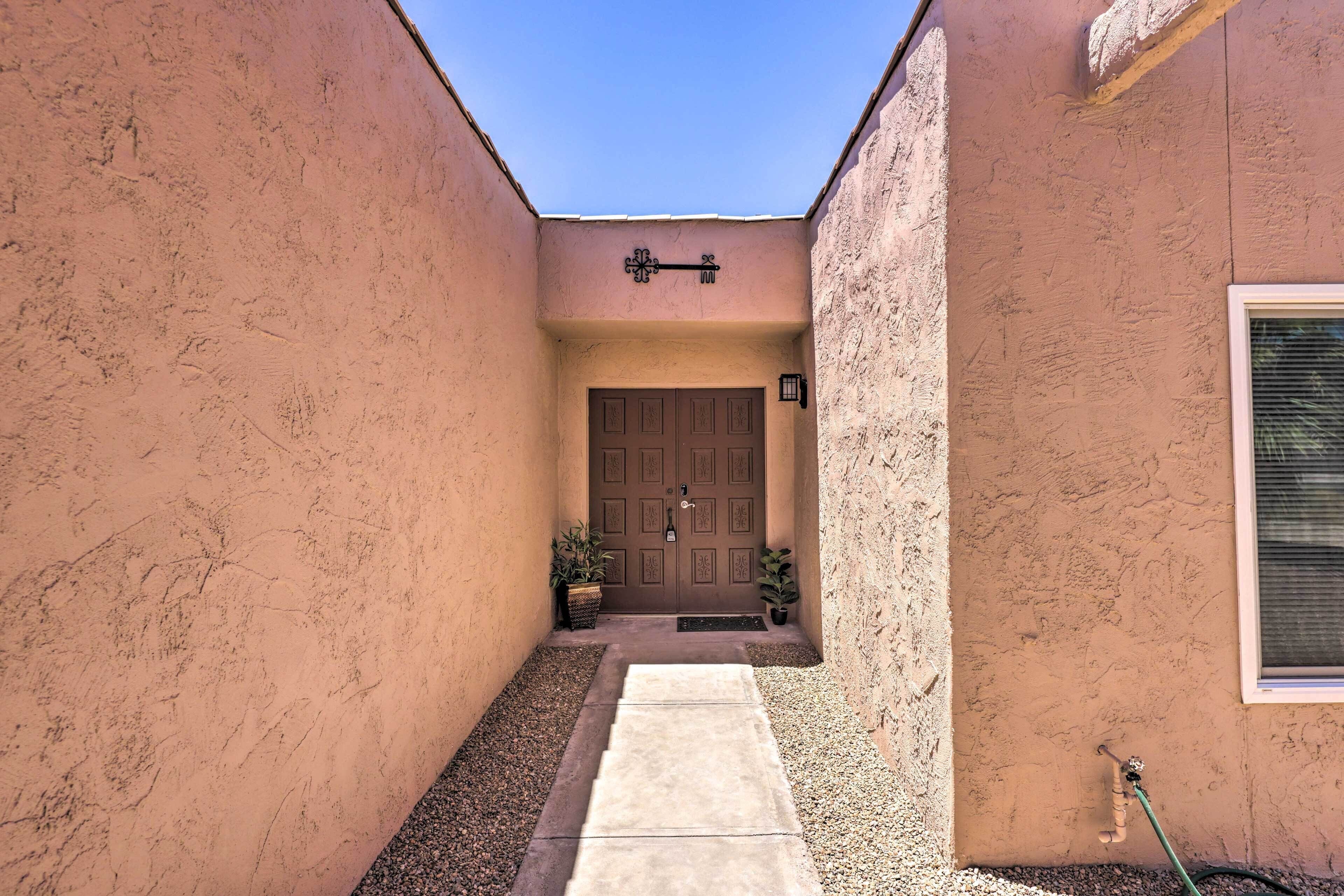 A narrow pathway leading to a door with a small garden area and a window on the right.