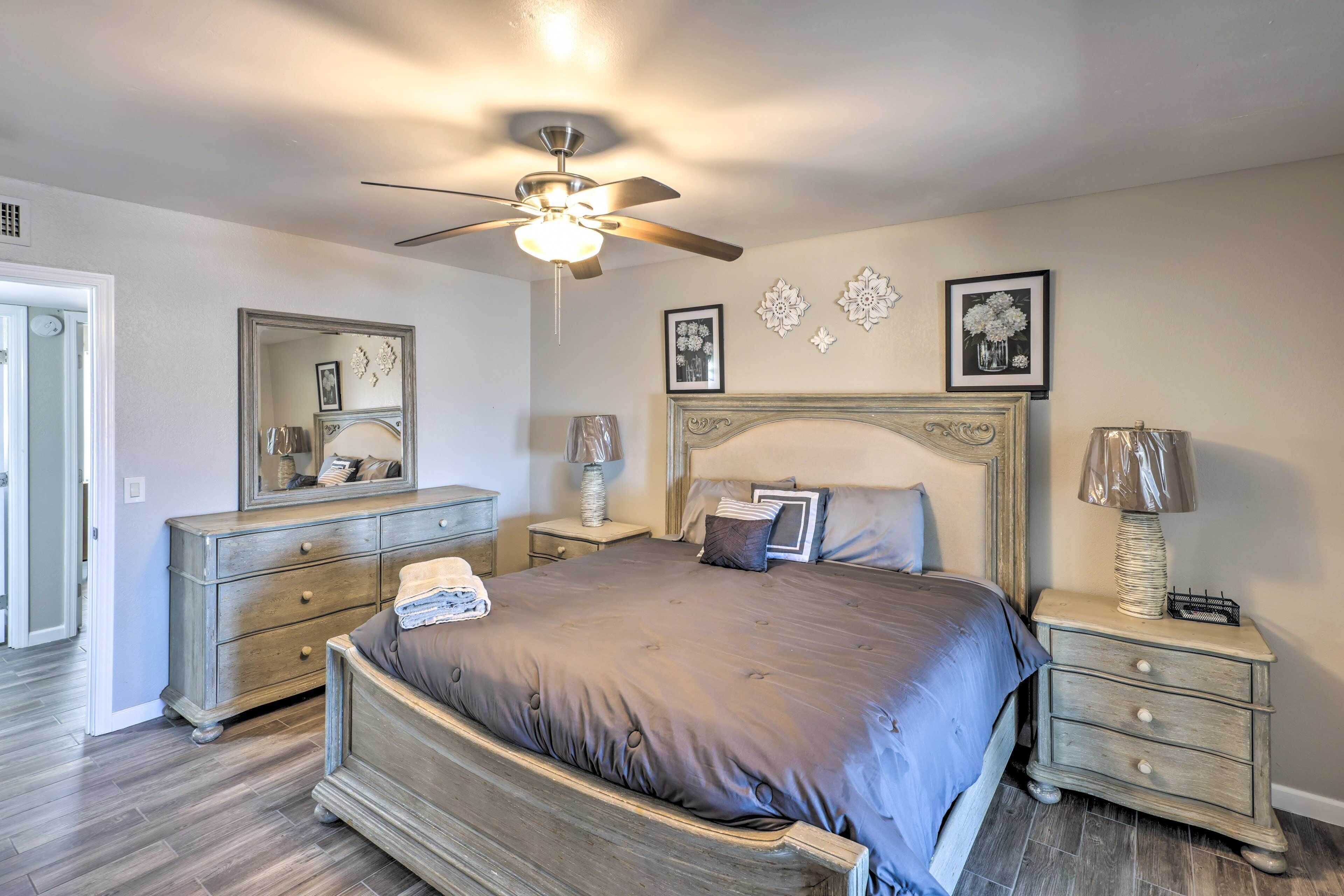 A bedroom with a large bed, a dresser, a nightstand, a ceiling fan, and wall decorations.
