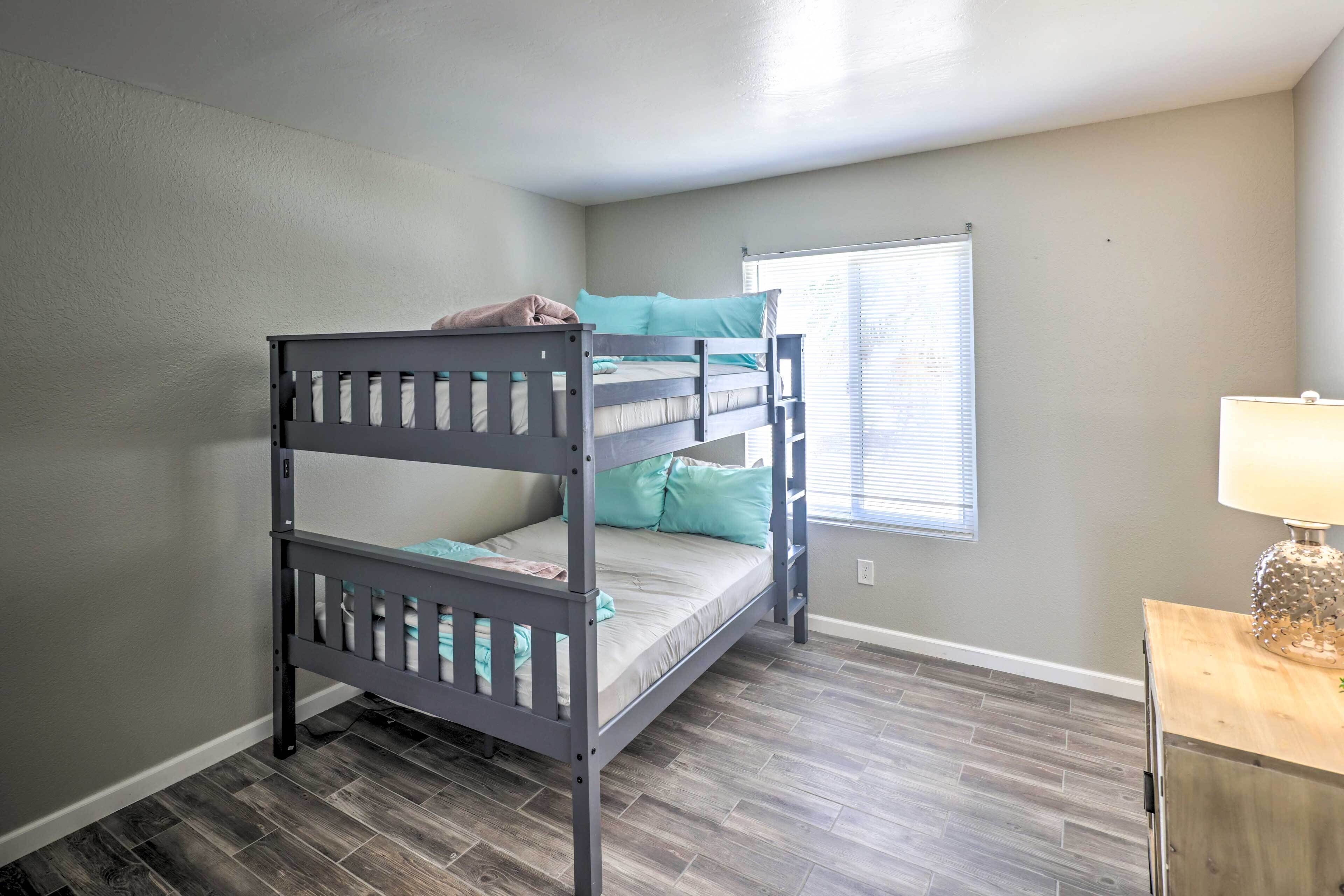 A bunk bed room with a window, a lamp, and a wooden nightstand.