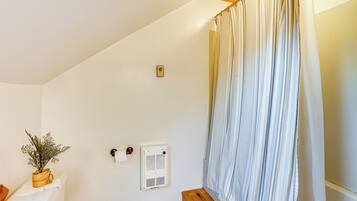 A bathroom with a white wall, a wooden ceiling, a white radiator, a towel rack, and a potted plant.