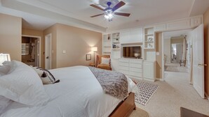 Une chambre à coucher comprenant un lit, un ventilateur de plafond, une commode et un dressing.
