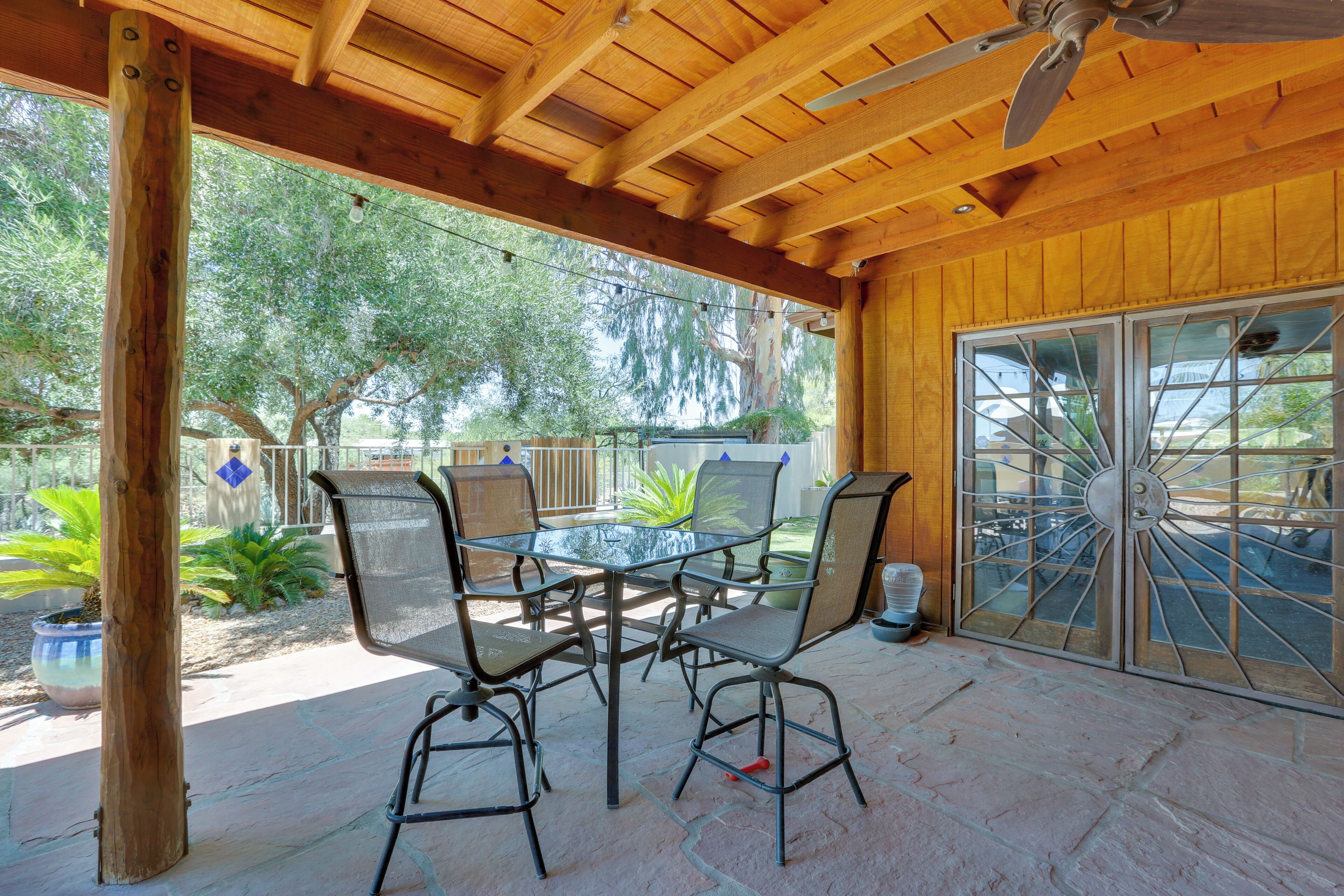 An outdoor patio with a wooden ceiling, a glass table, and metal chairs.