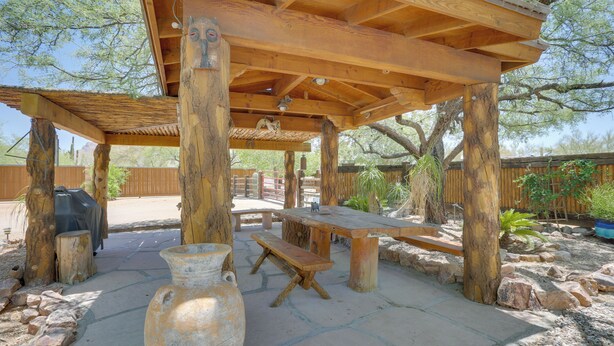 An outdoor wooden pergola with a picnic table and benches, surrounded by rocks and plants. - Tucson Home ~ 8 Mi to Saguaro National Park (Tucson)