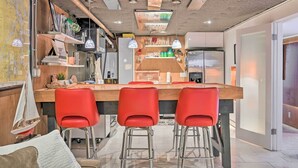 A modern kitchen with a central island, red bar stools, and a hanging sailboat decoration. - Edmonds Apartment With Private Wine Cellar! (Edmonds)