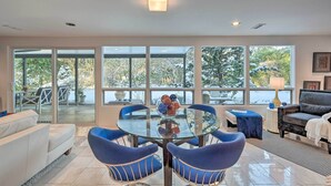 A modern living room with a glass table, blue chairs, a white sofa, and large windows offering a view of the outdoors. - Edmonds Apartment With Private Wine Cellar! (Edmonds)