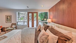 A modern bedroom with a large bed, a desk, and a chair. There are large windows with a view of greenery outside. - Edmonds Apartment With Private Wine Cellar! (Edmonds)