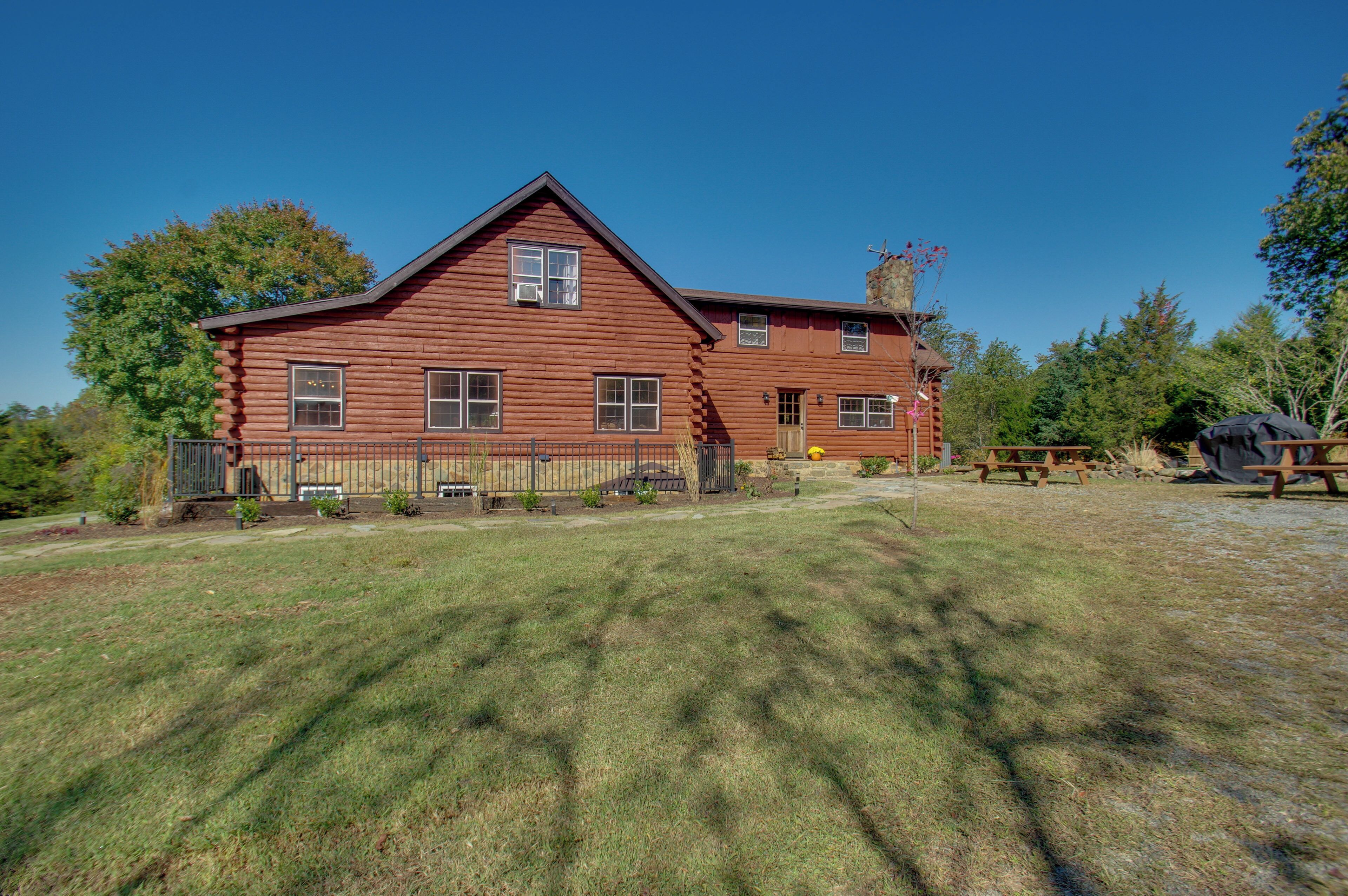 A large, two-story log cabin with a prominent chimney, surrounded by a well-maintained lawn and a fenced yard.