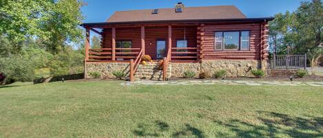 A log cabin with a stone foundation, a covered porch, and a clear blue sky.