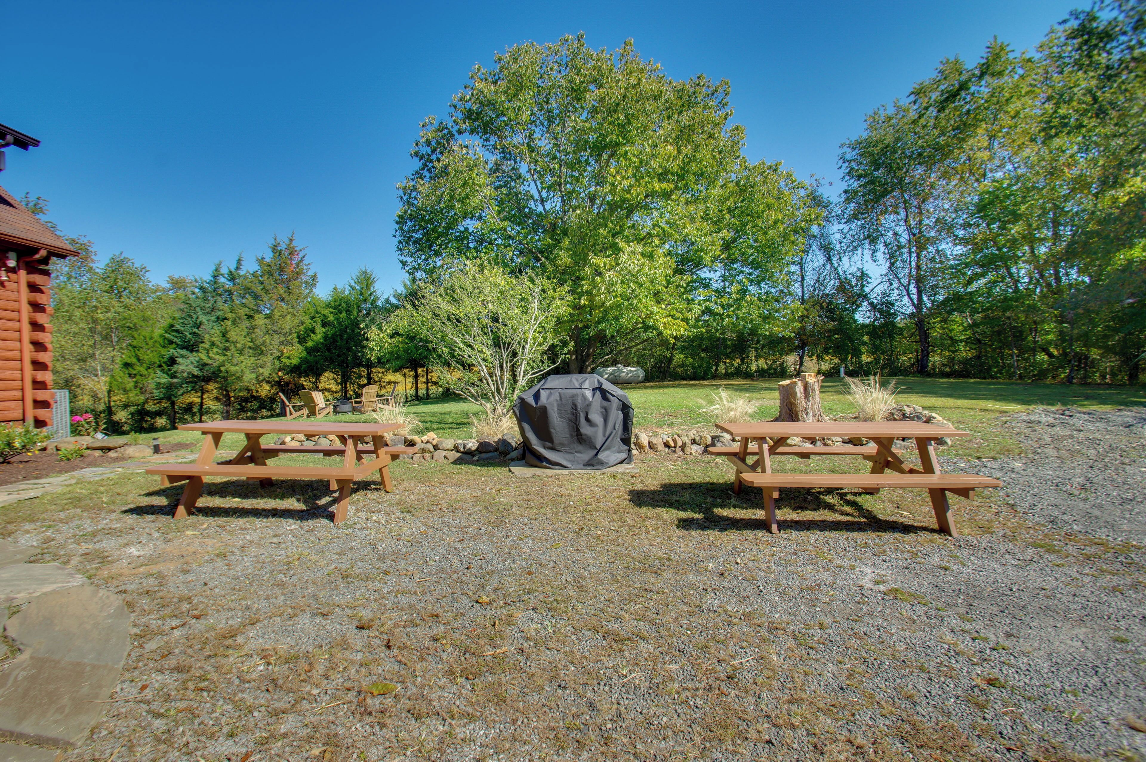 Un espace pique-nique équipé de deux tables de pique-nique en bois, d’un barbecue couvert et d’un muret en pierre.