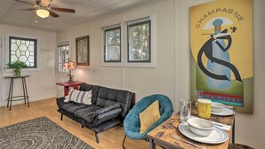 A dining area with a table set for two, a black leather sofa, a blue armchair, and a wall-mounted ceiling fan. - Guest Cottage on 1 Acre: 20 Mins to Asheville! (Black Mountain)