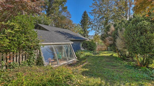 A house with a glass greenhouse attached to the side, surrounded by a garden with various plants and trees. - Guest Cottage on 1 Acre: 20 Mins to Asheville! (Black Mountain)