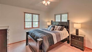 Une chambre à coucher comprenant un lit, deux tables de chevet, une commode, un ventilateur de plafond et deux fenêtres.