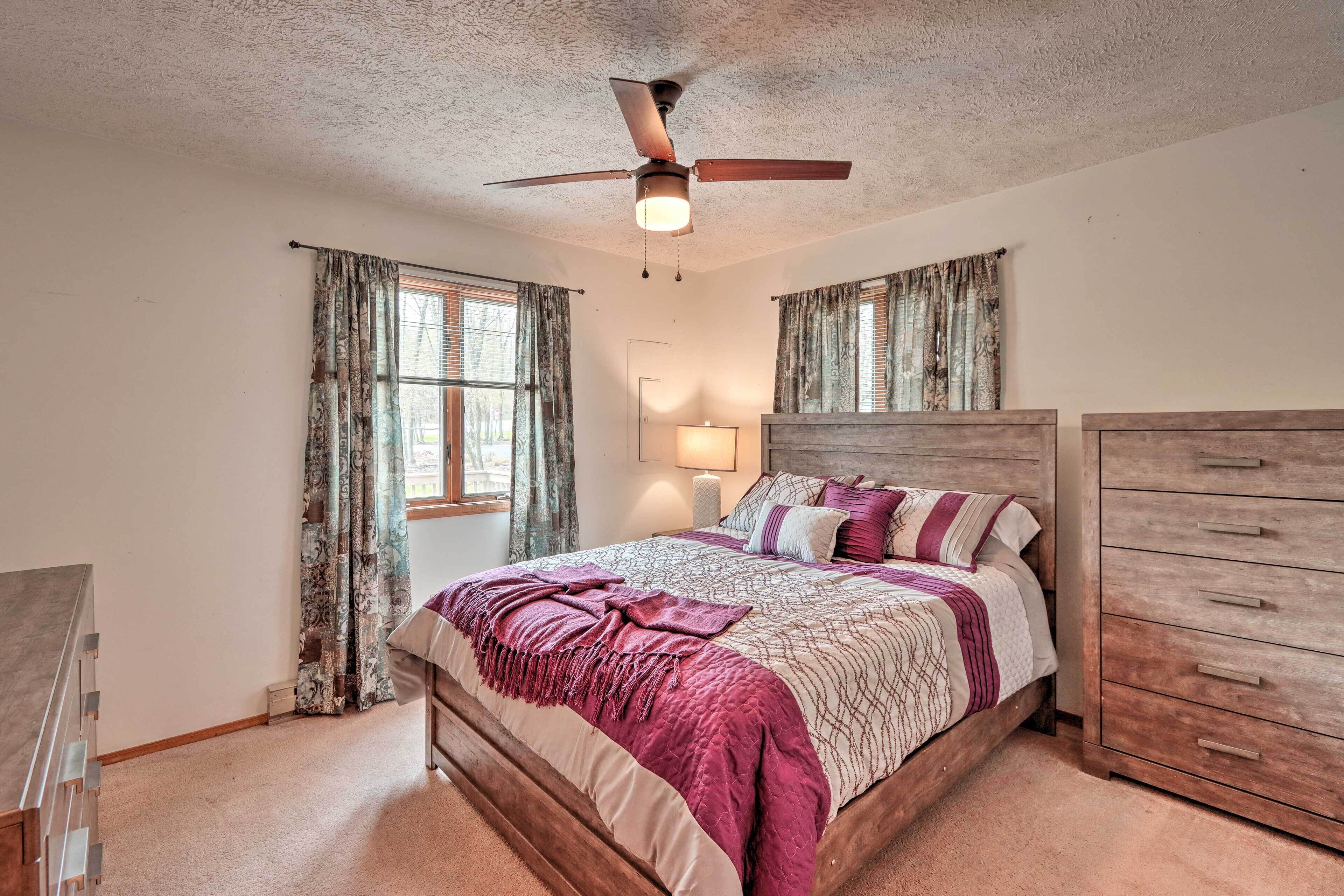 A bedroom with a wooden bed, a ceiling fan, a dresser, and curtains on the windows.