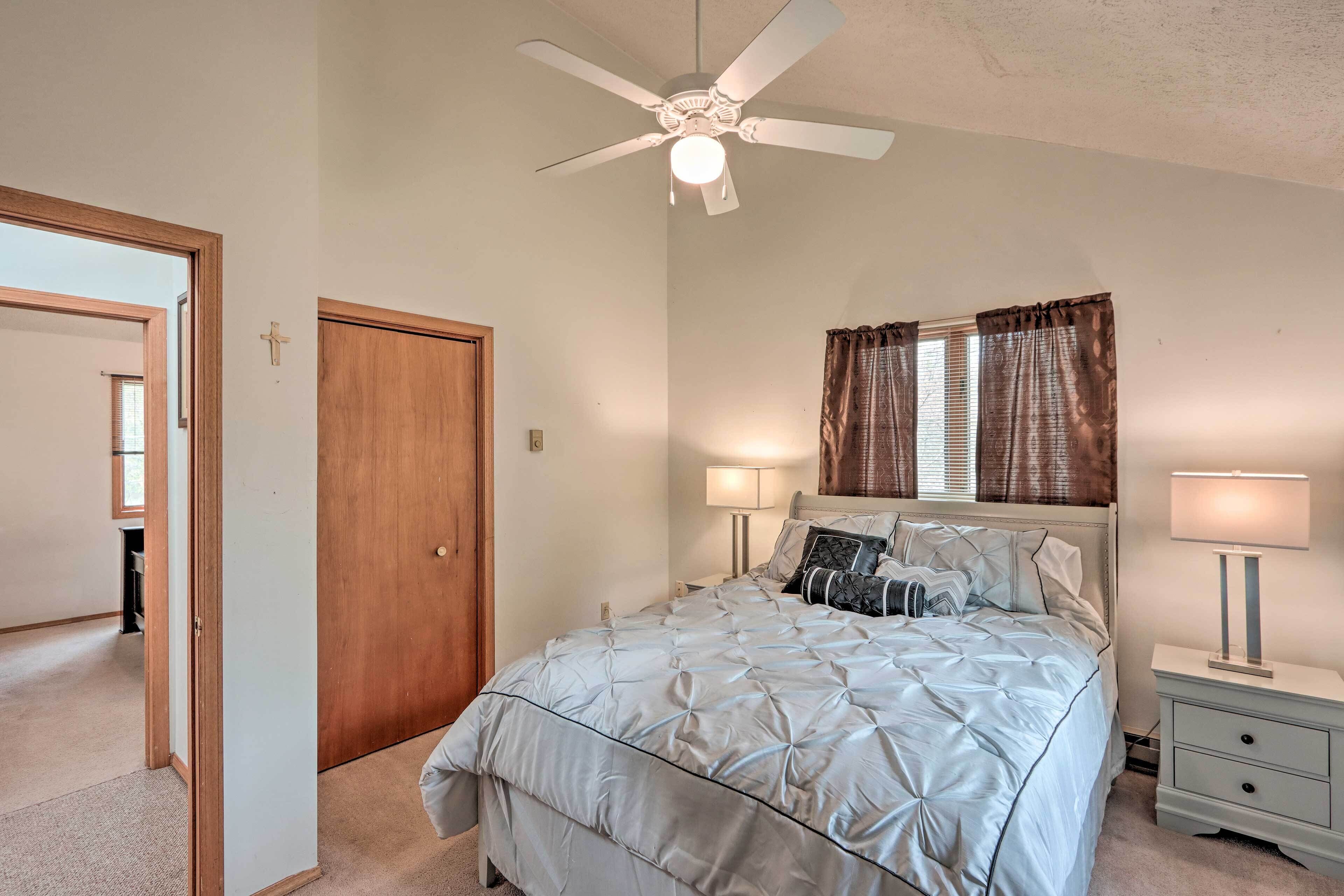 A bedroom with a bed, two bedside tables, a ceiling fan, and a window with curtains.