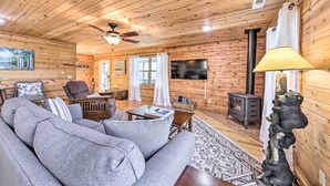 A cozy cabin interior with a sofa, a wooden ceiling, a fireplace, and a television. - Scenic Murphy Escape With Hot Tub & Fire Pit! (Murphy)