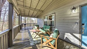 A covered porch with wooden furniture, a blue door, and a view of the surrounding trees. - Scenic Murphy Escape With Hot Tub & Fire Pit! (Murphy)