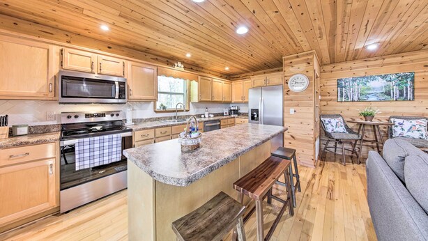 A wooden cabin kitchen with a granite countertop, stainless steel appliances, and a dining area with a bench and table. - Scenic Murphy Escape With Hot Tub & Fire Pit! (Murphy)