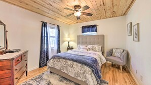 A bedroom with a wooden ceiling, a bed with a floral bedspread, a nightstand with a lamp, a chair, and a dresser. - Scenic Murphy Escape With Hot Tub & Fire Pit! (Murphy)