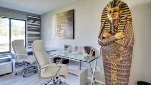 A modern office with a glass desk, white chairs, and a decorative Egyptian statue. - Bright Ormond Beach Home ~ 14 Mi to Daytona! (Ormond Beach)