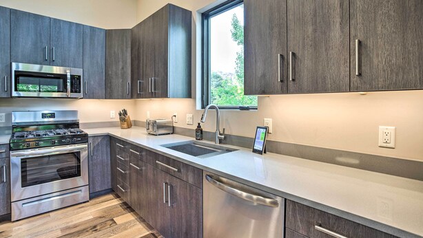 A modern kitchen with dark wood cabinets, stainless steel appliances, and a large window providing natural light. - Sleek & Modern Townhome, 3 Blocks to Main St! (Moab)