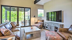 A spacious living room with a large sectional sofa, a coffee table, and a TV mounted on the wall. There is a sliding glass door leading to an outdoor patio area. - Sleek & Modern Townhome, 3 Blocks to Main St! (Moab)