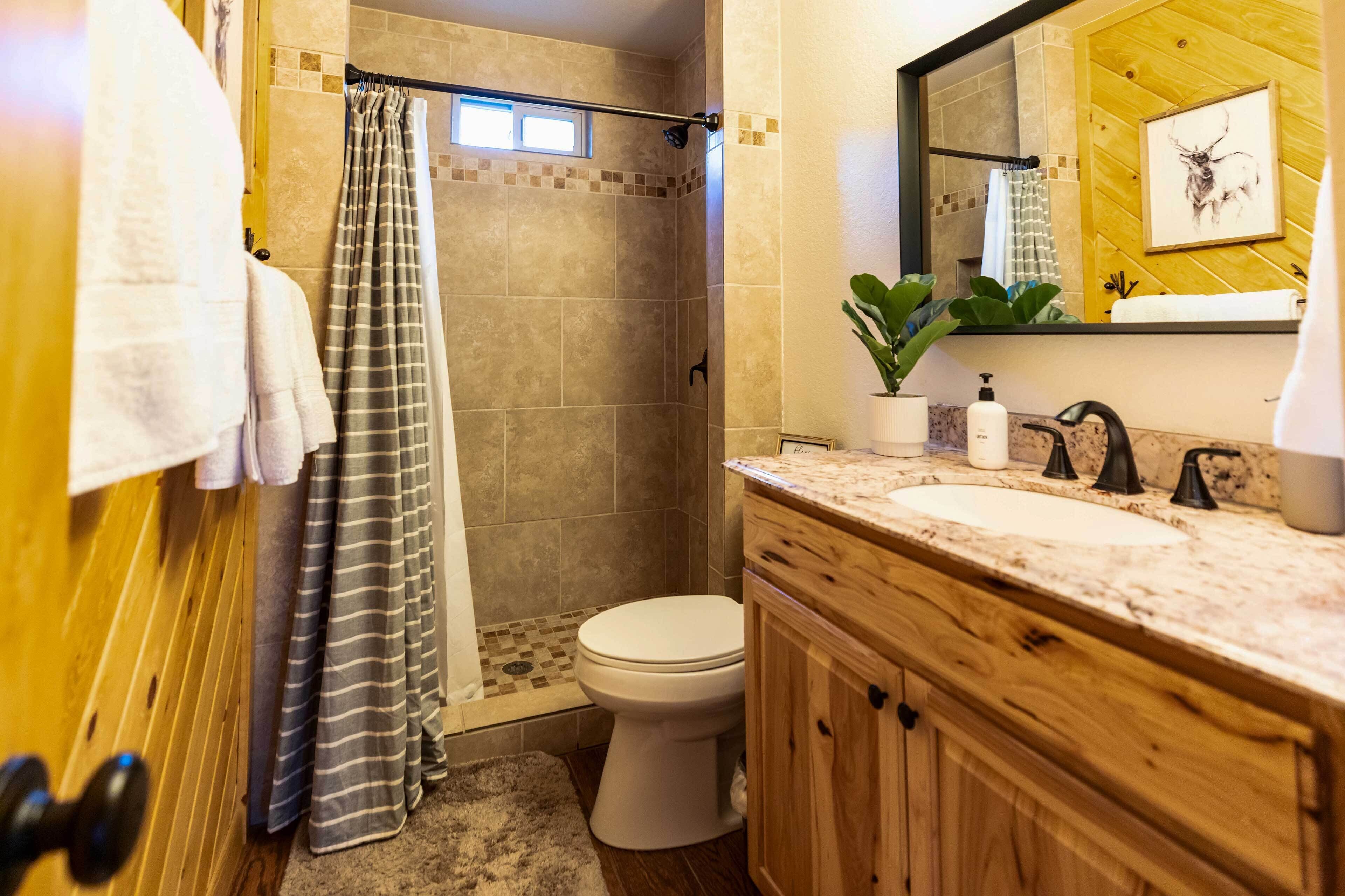 A bathroom with a shower, toilet, and wooden vanity with a sink.