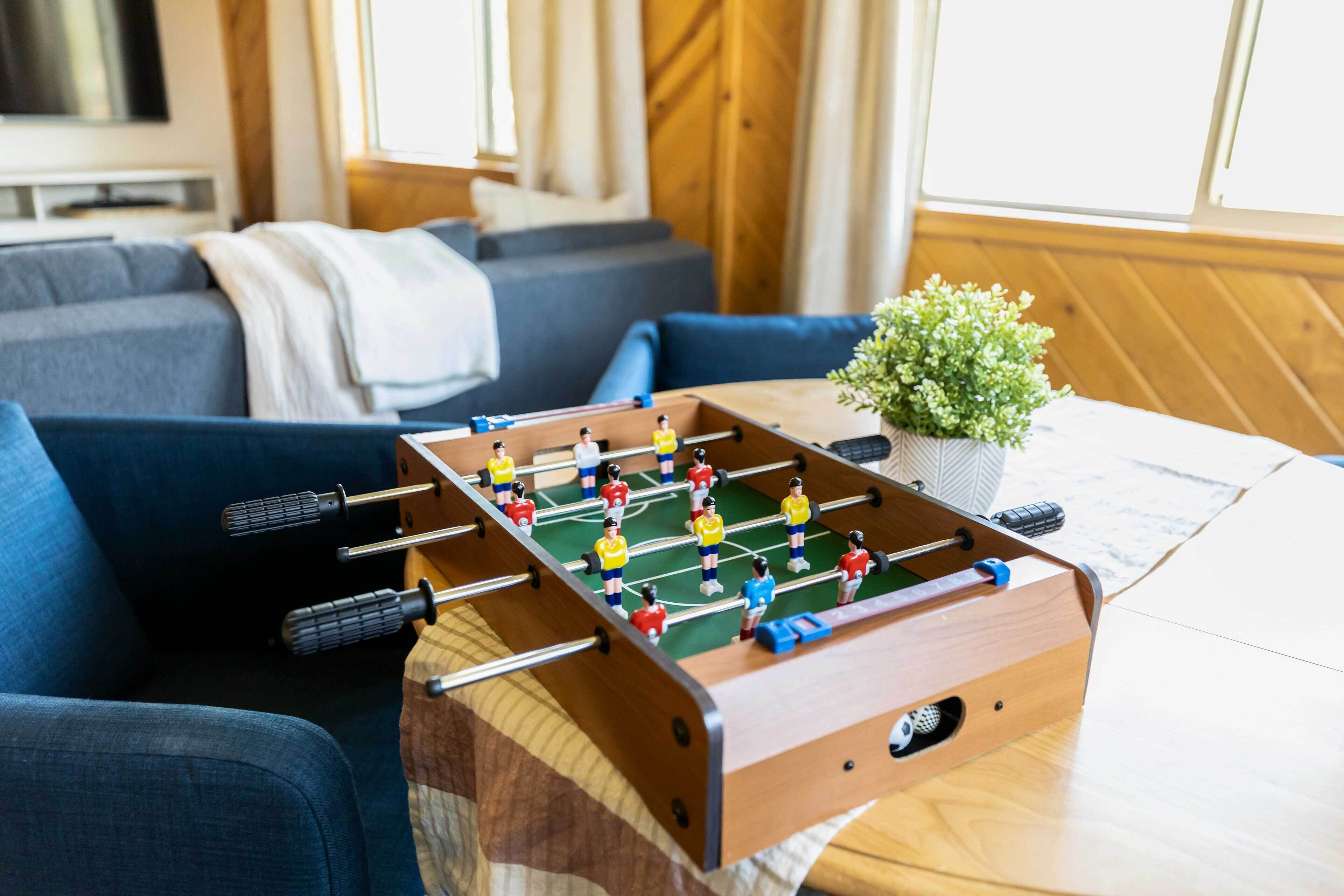 A foosball table in a living room with a sofa and a plant.
