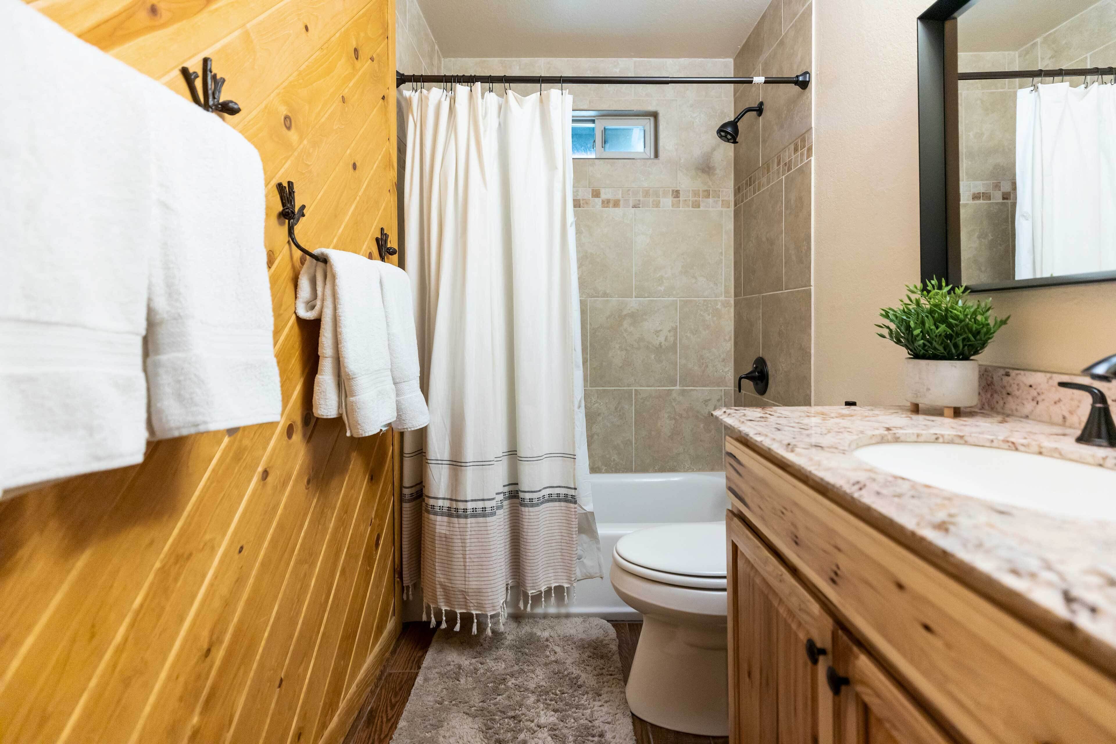Une salle de bain avec des murs en bois, une baignoire blanche, un rideau de douche, des toilettes et un lavabo avec un miroir.