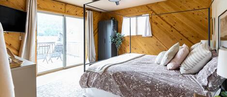 A bedroom with a bed, a ceiling fan, a large window, and a view of the outdoors.