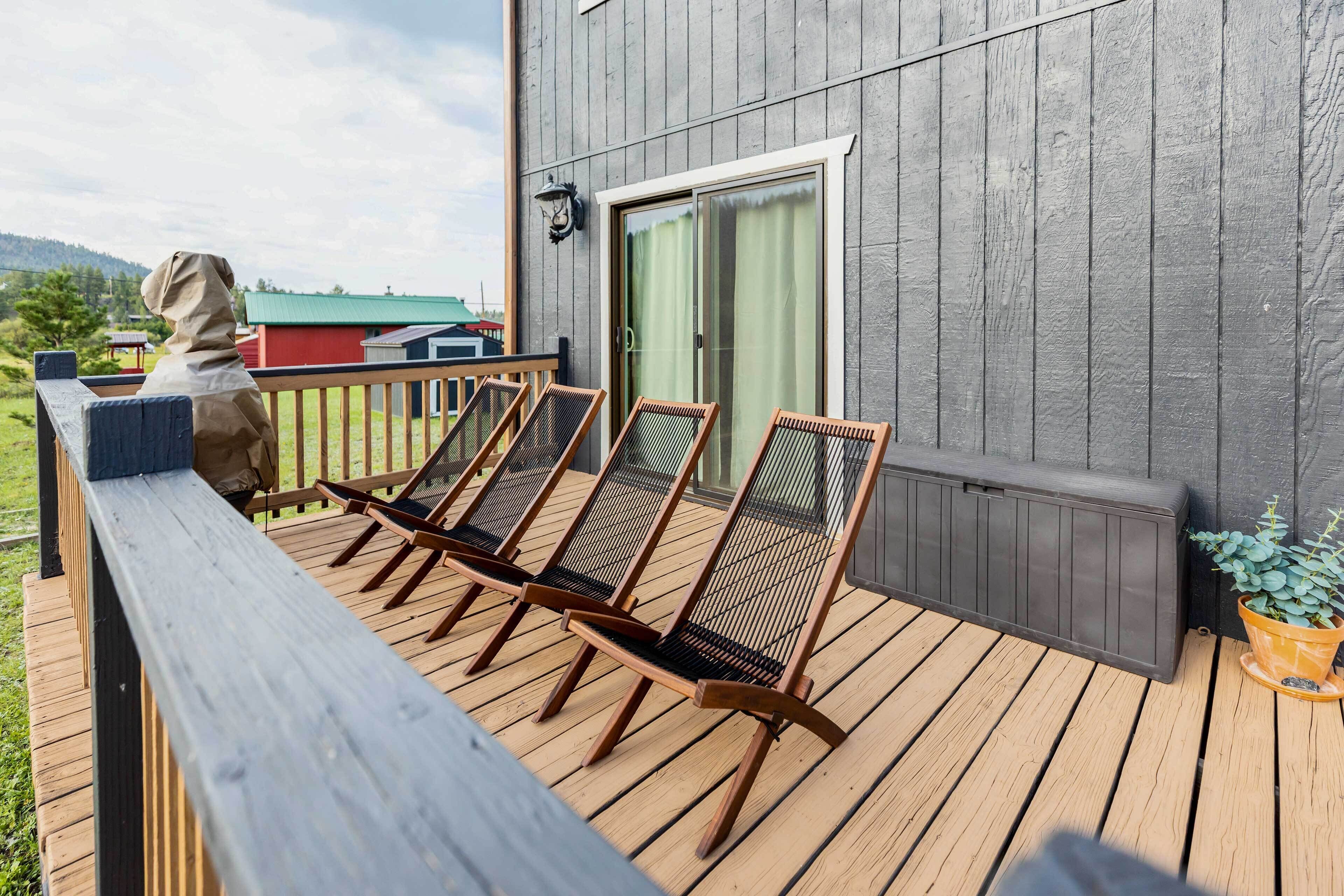 A wooden deck with four wicker chairs and a bench, a statue, and a potted plant.