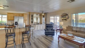 Amplia sala de estar con cocina, comedor con taburetes de bar, un sillón de cuero, sofá y un ventanal con vistas.