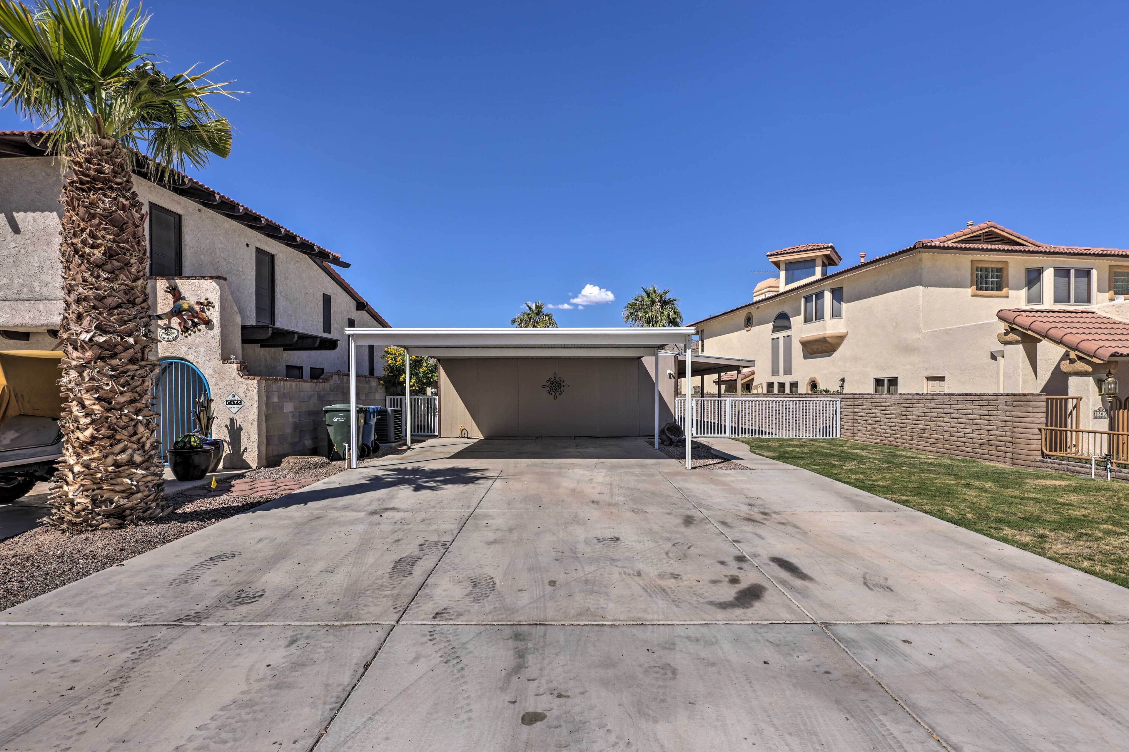 A covered patio area with a concrete floor, palm trees, and a clear blue sky.