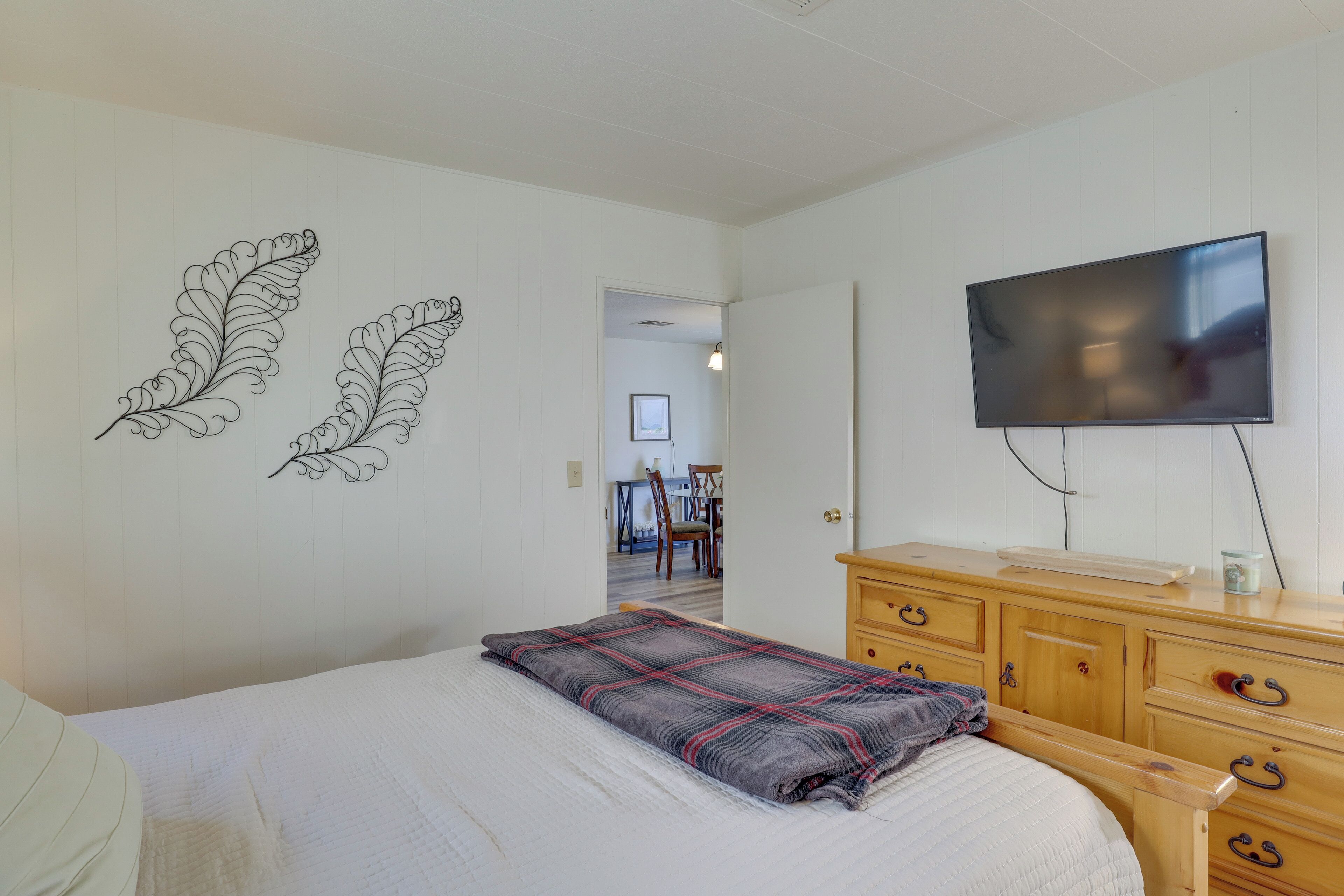 A bedroom with a bed, a wooden dresser, a television, and two wall art pieces.