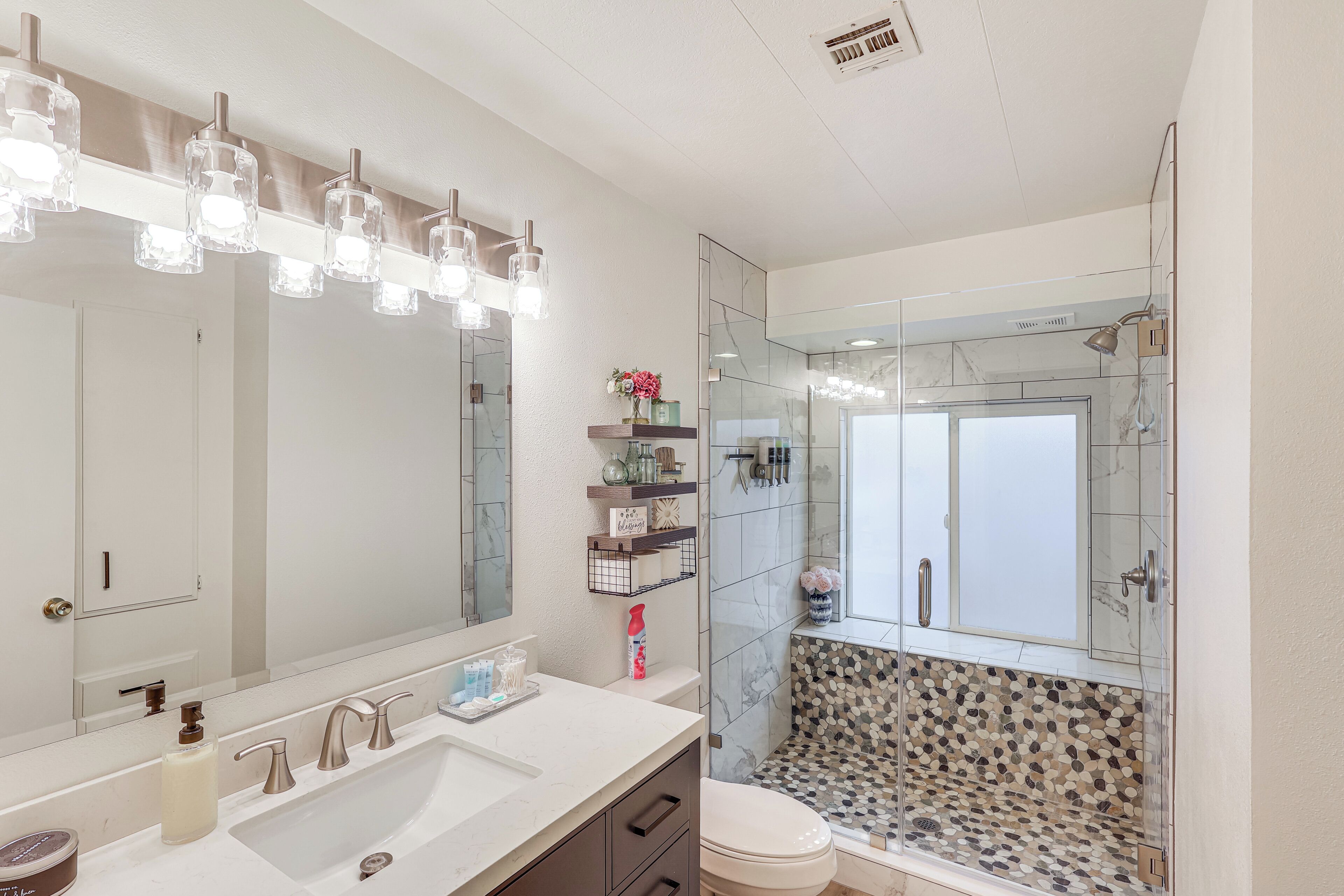 Une salle de bain moderne avec un grand miroir, un lavabo blanc doté de deux robinets et une douche séparée par une paroi de verre.