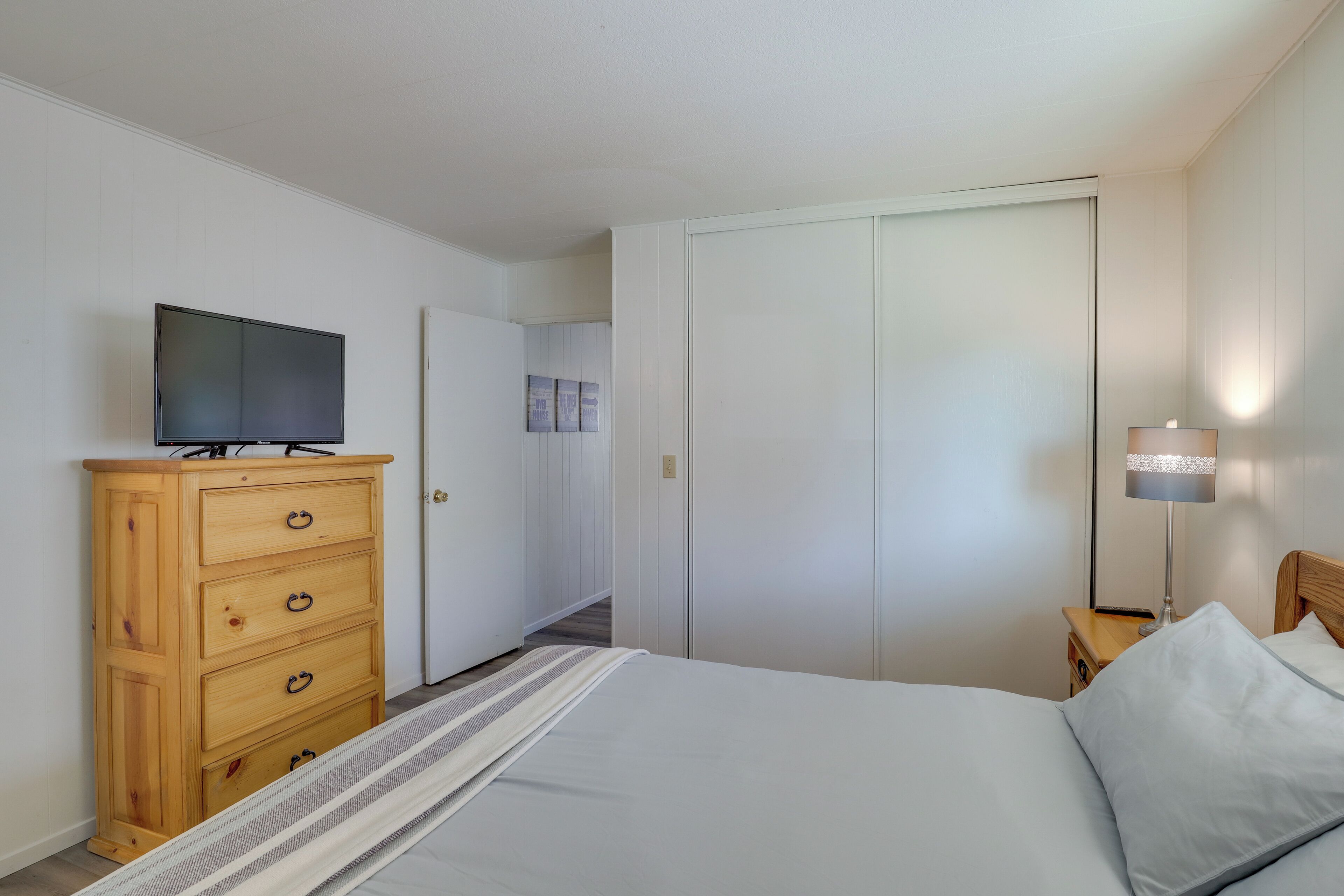 A bedroom with a bed, a wooden dresser, a television, a nightstand with a lamp, and a closet.