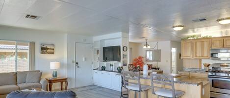 A modern kitchen with a central island, bar stools, and a dining area with a sofa and a lamp.