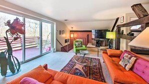 A spacious living room with a large sofa, a coffee table, and a green armchair. There is a sliding glass door leading to an outdoor area. - Creek Access & Deck: Runningwater Lancaster Gem (Lancaster)