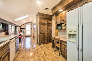 A kitchen with wooden cabinets, a refrigerator, and a dining area with a table and chairs. - Creek Access & Deck: Runningwater Lancaster Gem (Lancaster)