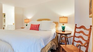 A neatly made bed with white bedding and a red pillow, a wooden chair, a small table with a lamp, and a wall-mounted shelf with a vase. - High-end Sapphire Retreat on Fairfield Lake! (Sapphire)