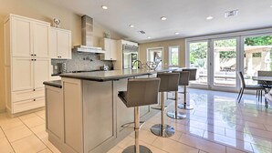 A modern kitchen with a central island, bar stools, and a dining area with a view of the outdoors. - Outdoor Kitchen: Desert Dream Home in Scottsdale! (Scottsdale)