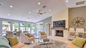 A spacious living room with a fireplace, comfortable seating, a television, and large windows offering a view of the outdoors. - Outdoor Kitchen: Desert Dream Home in Scottsdale! (Scottsdale)