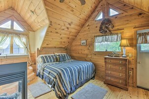 Un dormitorio acogedor con techo de madera, una cama con ropa de cama a rayas, un aparador y una decoración de cabeza de caballo montada.