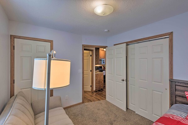 A bedroom with a bed, a lamp, a closet, and a door leading to a kitchen.