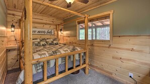 Une pièce de cabane en bois avec un lit superposé, un ventilateur de plafond, une fenêtre et un panneau mural.