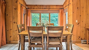 Een eetzaal met houten lambrisering, een grote tafel met stoelen, een raam met gordijnen en een plafondlamp.