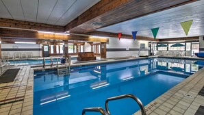 Ein Hallenbad mit klarem Wasser, Holzbalken an der Decke und einem Rettungsschwimmerstuhl.